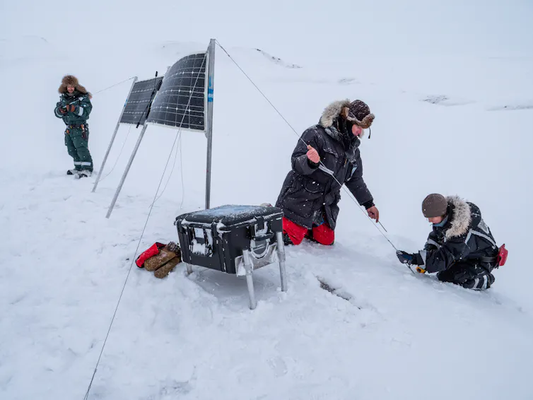 three people setting up a time-lapse camera in the snow
