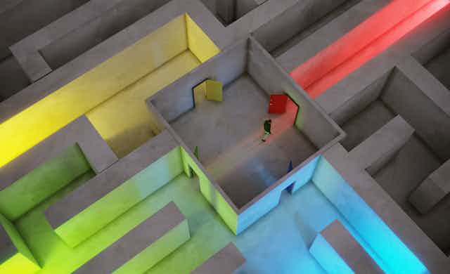 Bird's-eye view of a man walking through a maze with multicolored hallways.