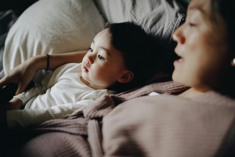 A woman lies next to an infant looking at a book.