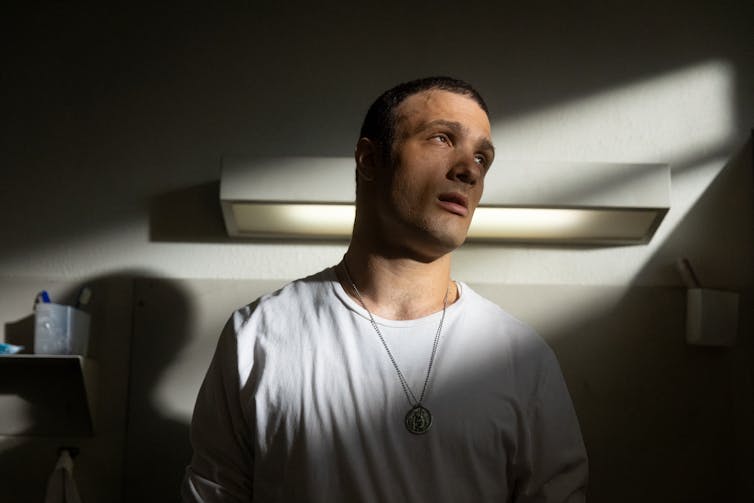 Film still: a man sits in a shard of light.