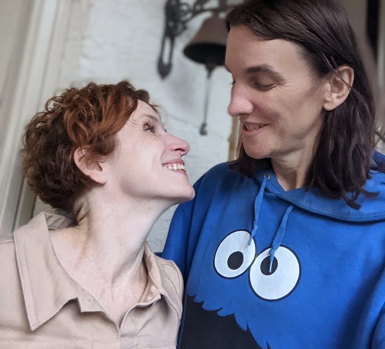 a red-haired woman smiling up at her girlfriend, who wears a Cook