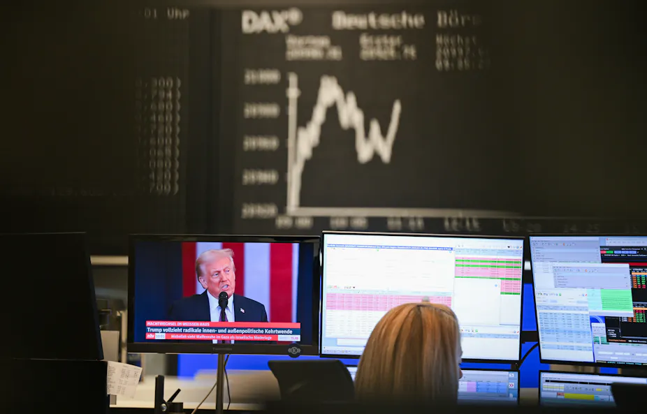 A screen shows Donald Trump as a trader looks at other screens showing market data.