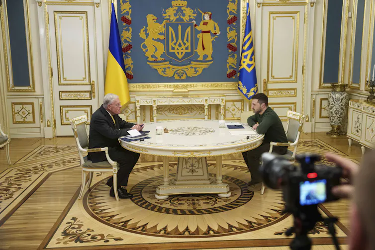 two men sit across from each other at a round table in a very ornate room