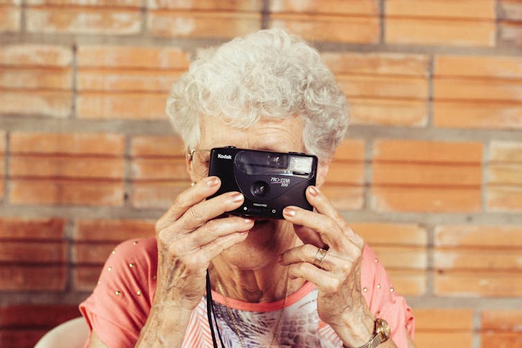 elderly woman holding digital camera in front of face