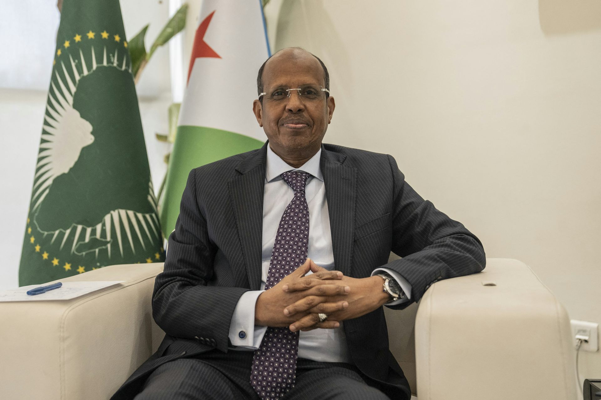 Man wearing grey suit, seating in front of two flags