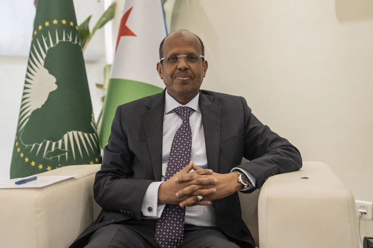 Man wearing grey suit, seating in front of two flags
