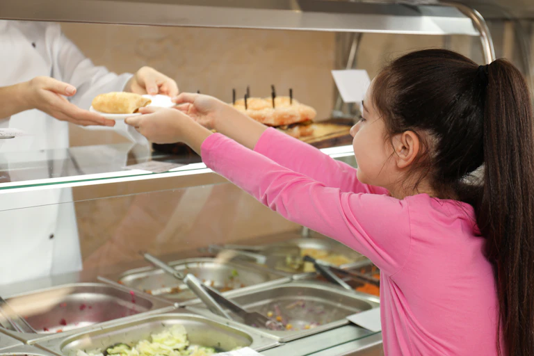 Woman gives a plate of food to a girl in a school canteen.