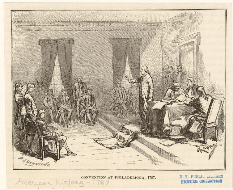 Men in a high-ceilinged room, some writing, some talking.