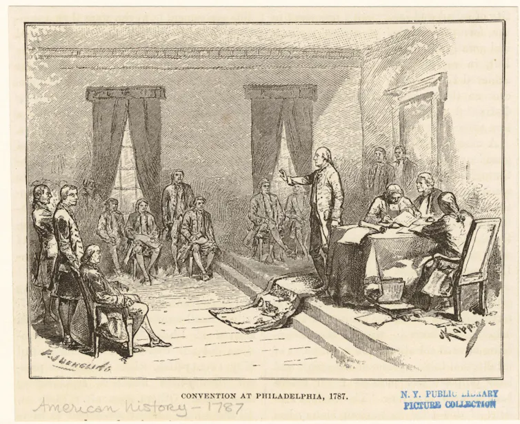 Men in a high-ceilinged room, some writing, some talking.