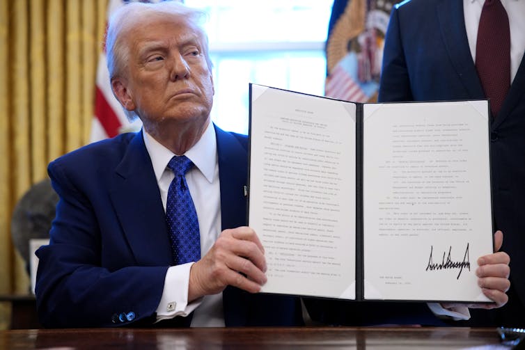 A man at a desk holding a folder with white paper inside it.