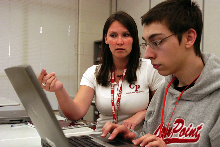 Teacher and student at a desk with laptop.