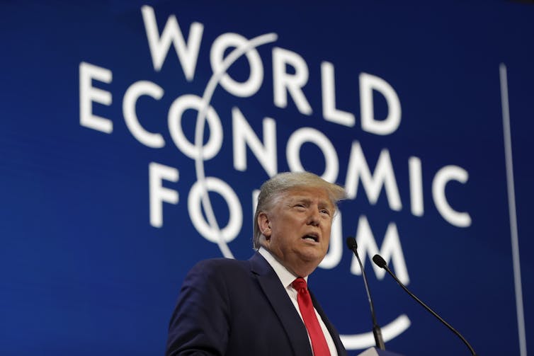 A man stands in front of a microphone beneath 'World Economic Forum' sign