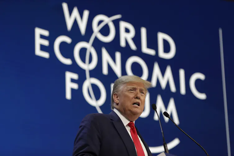 A man stands in front of a microphone beneath 'World Economic Forum' sign