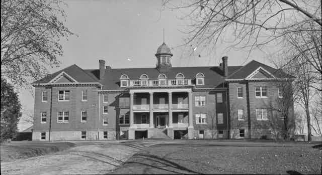 A black and white photo of a large brick building surrounded by trees