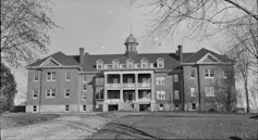 A black and white photo of a large brick building surrounded by trees