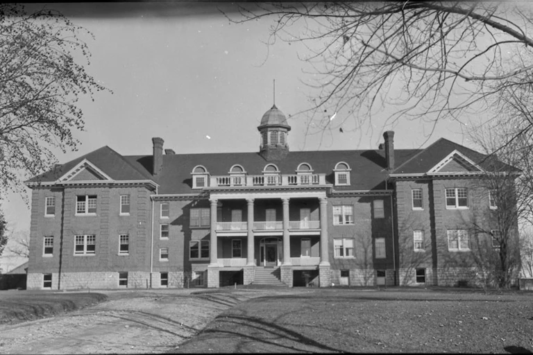 A black and white photo of a large brick building surrounded by trees
