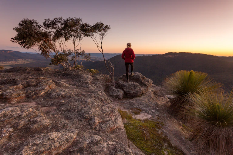 Woman in red jacket standing on top of mountain and looking out at the view.