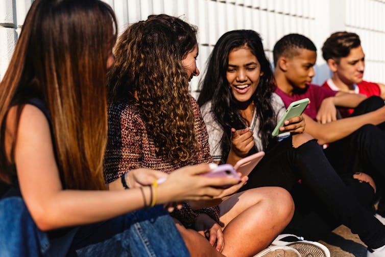A group of teenagers sit together and chat while using their smartphones