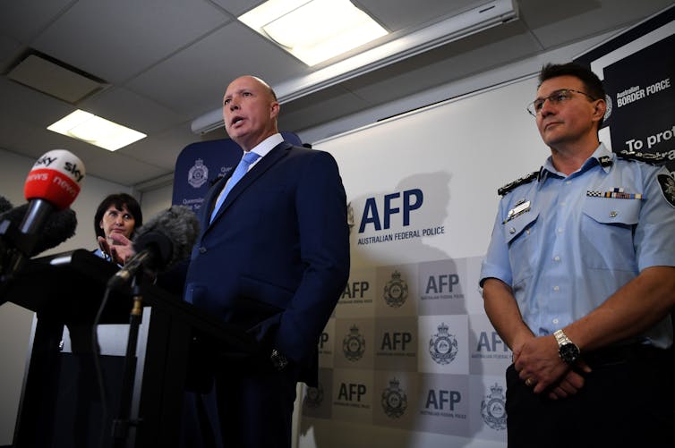Man in suit gives a press conference standing next to police officer in uniform.