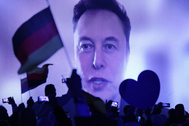 A mans' face is seen on a large screen in front of a people waving flags.