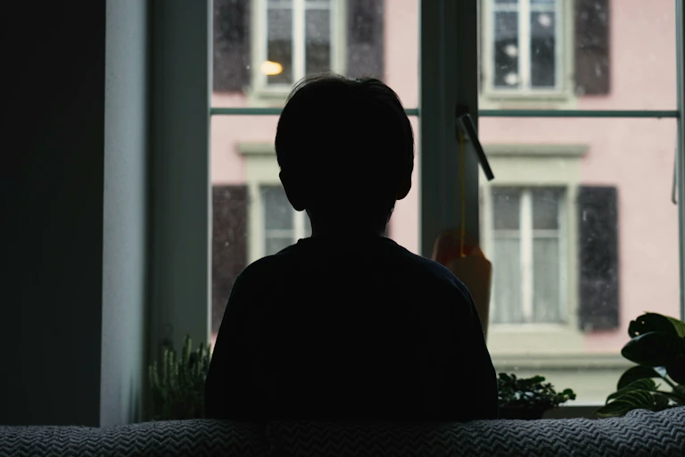 A child's silhouette is set against a window displaying an urban scene.