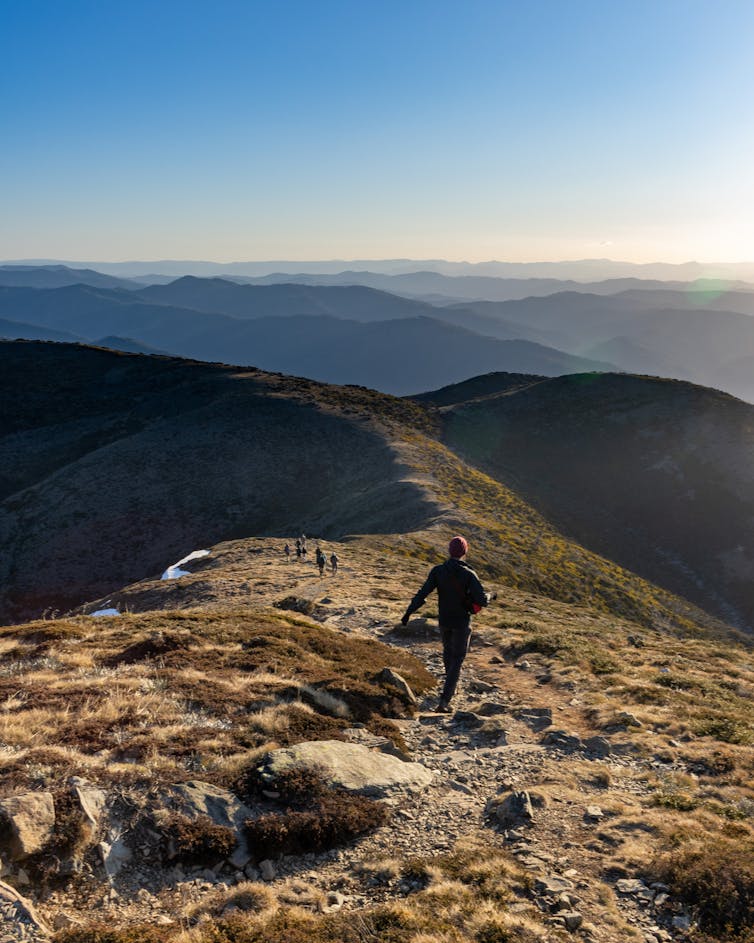 Hikers walk down a ridge on Mt Feathertop, the Australian Alps stretches to the horizon.