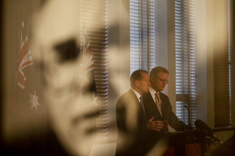 Tony Abbott and Scott Morrison standing in the reflection of John Howard.