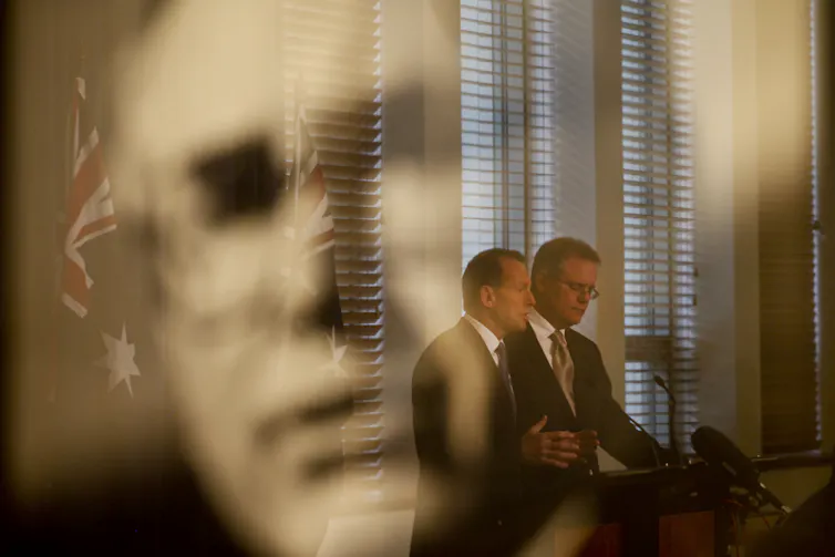 Tony Abbott and Scott Morrison standing in the reflection of John Howard.