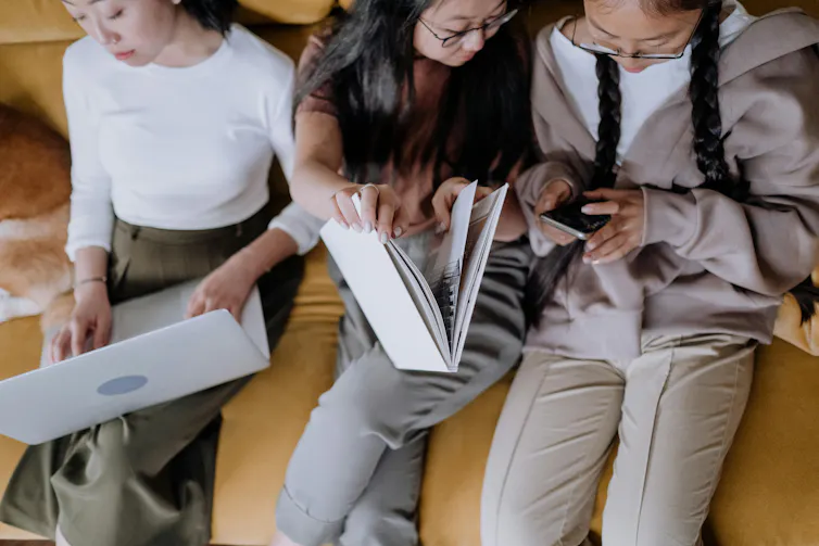 three girls - with a laptop, a book and a phone