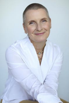 a smiling woman in a white shirt with an almost-shaved head