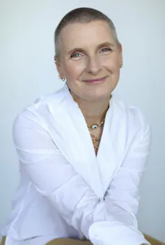 a smiling woman in a white shirt with an almost-shaved head