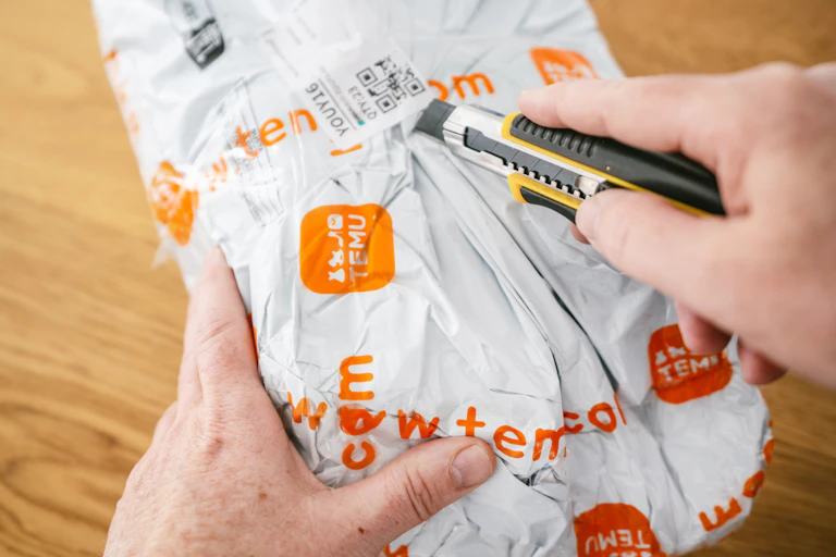 une personne ouvre un colis temu avec un cutter
