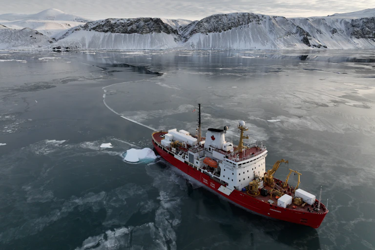 Un brise-glace s'éloigne d'une falaise glacée.
