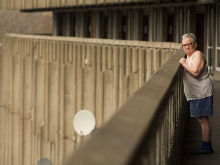 Elderly man leans against a concrete barrier.