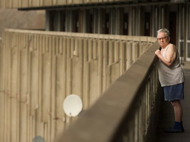 Elderly man leans against a concrete barrier.