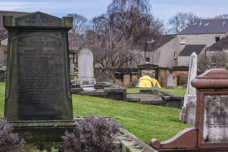 A tent pitched in a cemetary next to houses.
