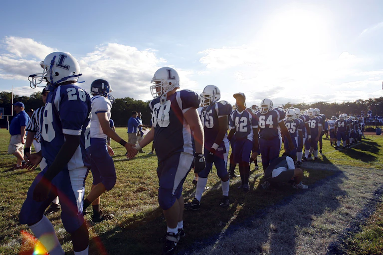 boys in football clothing line up on field under blue skies to shake other team's hands