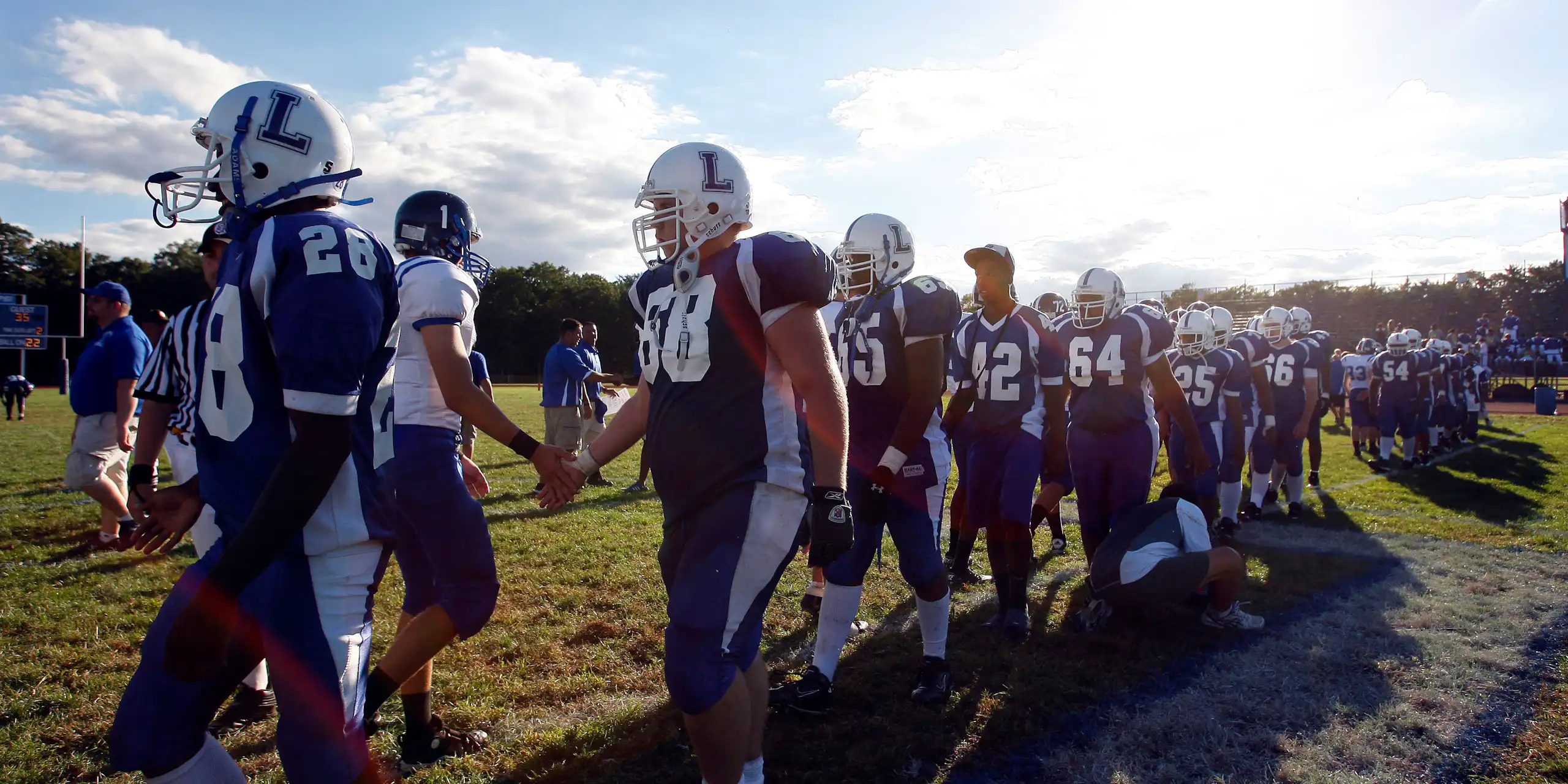 boys in football clothing line up on field under blue skies to shake other team's hands