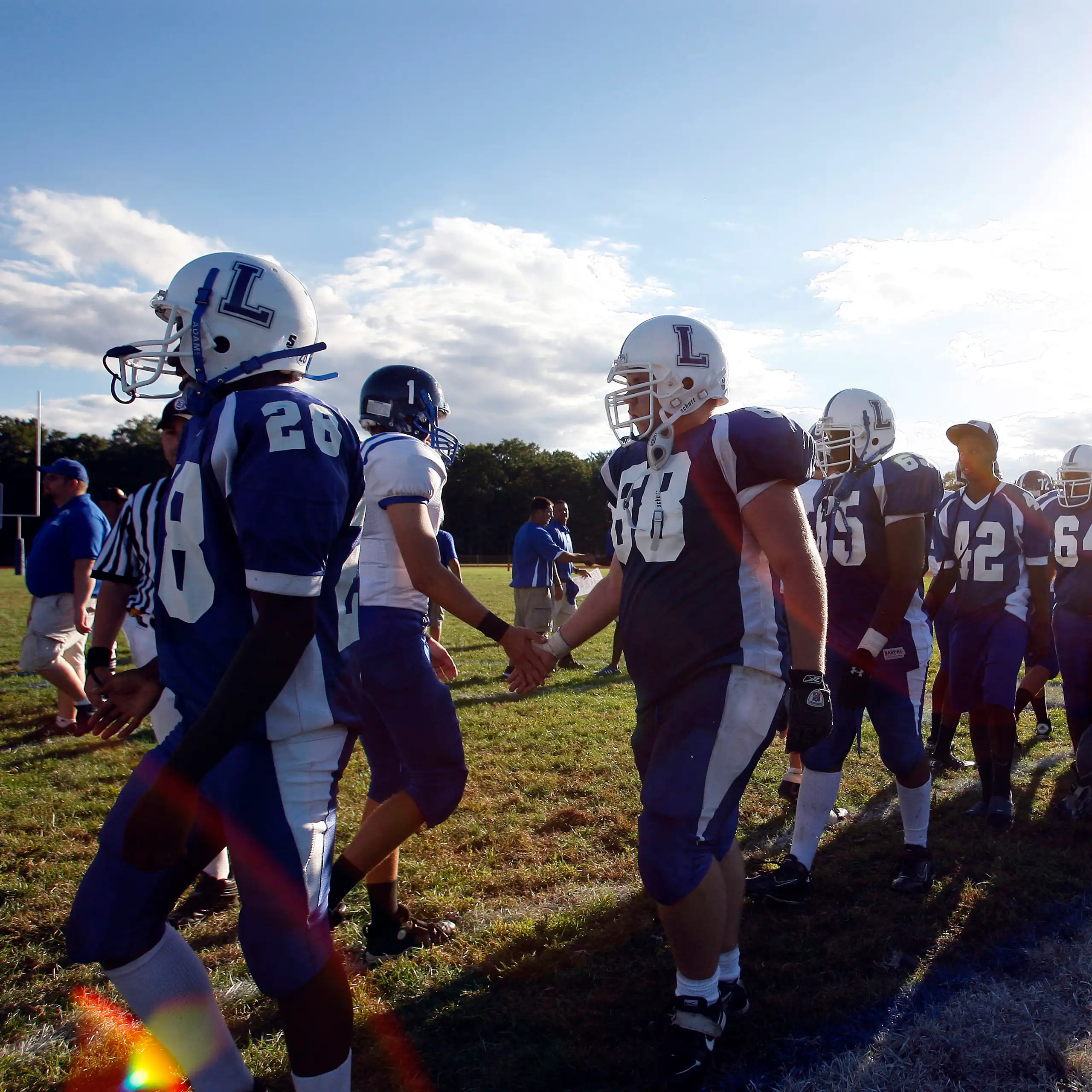 boys in football clothing line up on field under blue skies to shake other team's hands