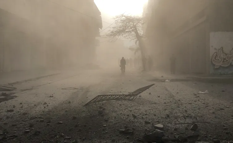 A man walks down a street in a loud of dust.