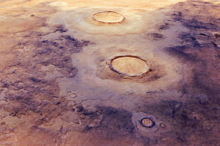 Uma paisagem laranja e roxa pontilhada por duas grandes crateras de impacto.