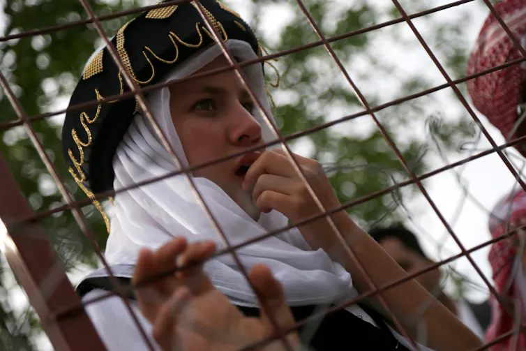 A young girl looks through a wire fence.