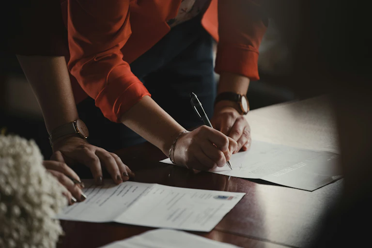 Two sets of hands lean on a table to sign documents