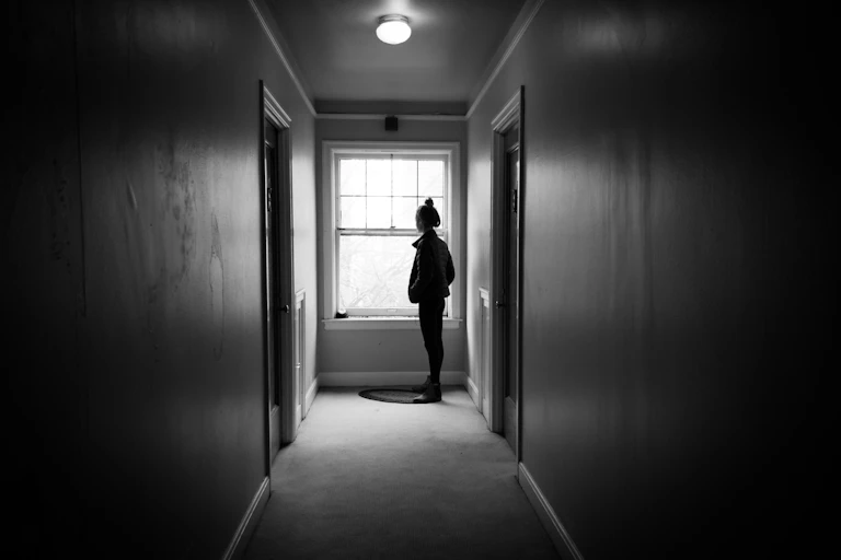 A woman in silhouette looks out of a window.