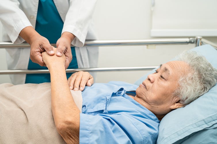 Doctor holds hands of an elderly woman in a hospital bed.