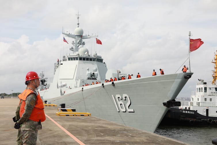 Chinese warship docked at a harbour with a guard standing to attention.