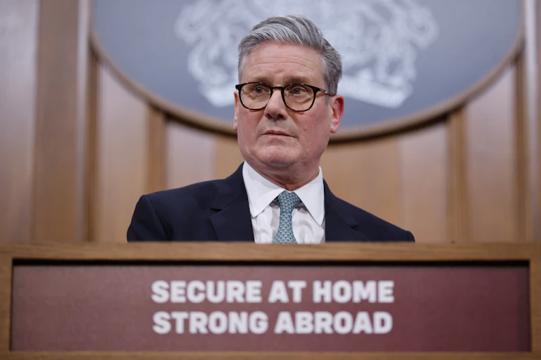 Starmer standing behind a podium that reads 'secure at home, strong abroad'
