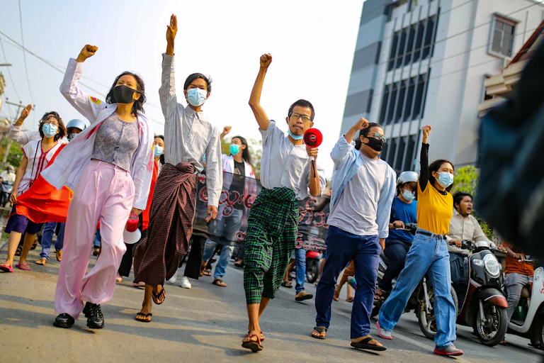 Young Myanmar citizens march down a road in protest.