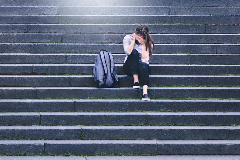 Girl sat alone with rucksack on steps outside