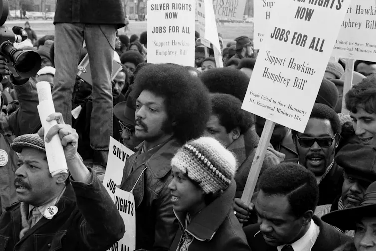 Black-and-white image of a protest march for 'jobs for all,' featuring a young Jesse Jackson front and center